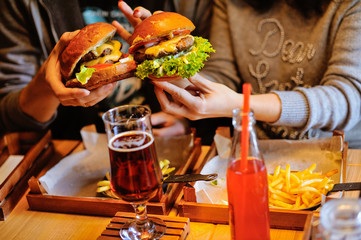 Woman and man hold burgers in their hands. Fresh burger cooked on a barbecue in kraft paper. American food. Nearby are drinks.