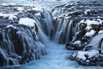 Amazing Nordic scenery of frozen waterfalls and river flowing through rough volcanic terrain covered with snow in Iceland
