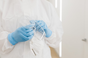 Protective medical goggles in the hands of a doctor in the white corridor of the hospital during covid. Blue medical gloves.