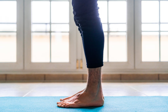 Low angle side view of crop barefoot male athlete in active wear standing in start position while training alone on sports mat against window in light spacious room at home