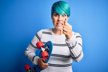 Young skater woman with blue fashion hair holding skateboard over blue isolated background annoyed and frustrated shouting with anger, crazy and yelling with raised hand, anger concept