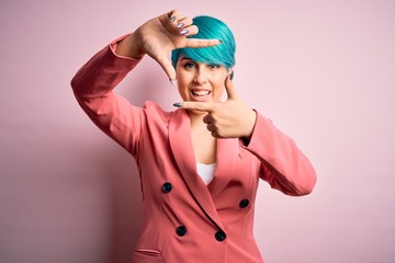 Young beautiful businesswoman with blue fashion hair wearing jacket over pink background smiling making frame with hands and fingers with happy face. Creativity and photography concept.