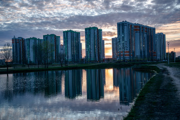 Fototapeta na wymiar Beautiful view of the reflection of apartment buildings in a lake at sunset. Picturesque sky at sunset. Living complex Sofia in St. Petersburg.