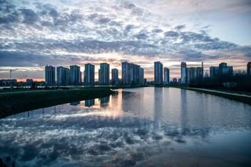 Fototapeta na wymiar Stunning sunset view with beautiful sky above the high-rise buildings and reflection in the lake. Residential complex Sofia St. Petersburg.