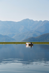 A beautiful view at a lonely boat in the middle of the lake Skadar with blue mountain view at background in Montenegro National Park, famous tourist attraction.