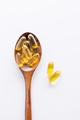 Fish fat oil capsules Omega-3  in wooden spoon on white background, top view