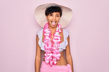 Young beautiful african american tourist woman wearing bikini and hawaiian lei flowers sticking tongue out happy with funny expression. Emotion concept.