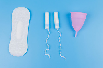 Sanitary pad, tampons and menstrual cup on blue background. Top view. Concept of critical days, menstruation, feminine hygiene