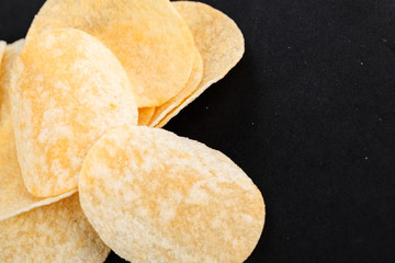 Classic potato chips. Fast food snack isolated on black background. A pile of crispy chips close-up as a background. Unhealthy food.