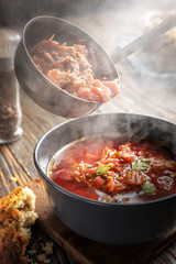 Borsch is poured into a bowl from a ladle from which steam, a traditional Ukrainian vegetable soup made from beets, carrots, tomatoes, potatoes, cabbage, herbs and garlic, close-up, shallow depth of