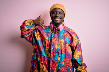 Young handsome african american man wearing colorful coat and cap over pink background smiling doing phone gesture with hand and fingers like talking on the telephone. Communicating concepts.