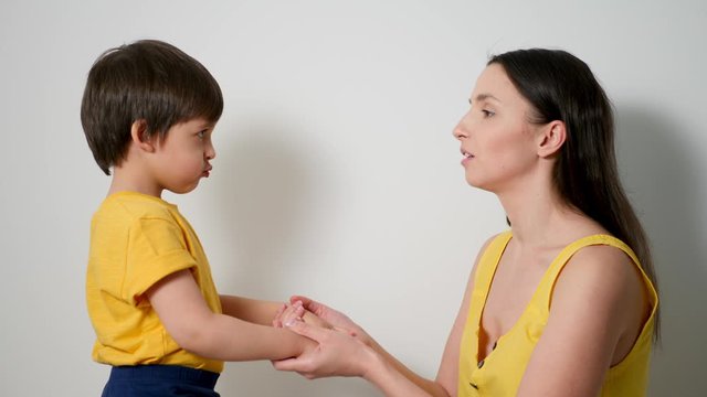 mother with her son a child of three years in yellow t-shirts, stands against a white wall in the studio and wants to kiss her