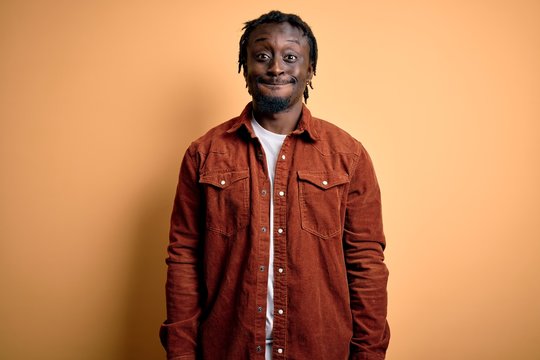 Young handsome african american man wearing casual jacket standing over yellow background puffing cheeks with funny face. Mouth inflated with air, crazy expression.