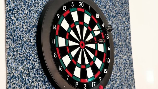 Throwing three darts at the board - aiming at bullseye and hitting the outer bullseye once. Shot from an approximate 45 degrees angle