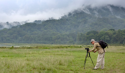 man with a camera on a tripod on a background of a mountain with a tropical forest. Bali. Indonesia.