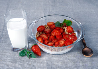 Muesli with yogurt and strawberries in a glass bowl, next to a glass of milk and a wooden spoon.