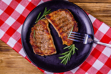 Plate with roasted steaks and rosemary twigs on a wooden table. Top view