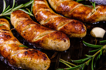 Roasted sausages with rosemary twigs and garlic in a cast iron grill pan