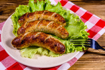 Plate with roasted sausages and lettuce leaves on a wooden table