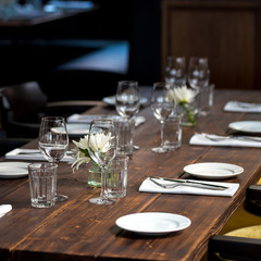 Glasses, flowers, fork, knife served for dinner in restaurant with cozy interior, retro film filter effect	