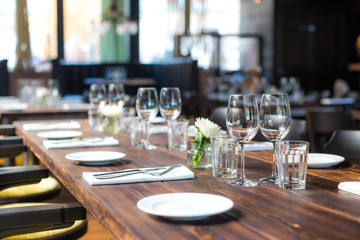 Glasses, flowers, fork, knife served for dinner in restaurant with cozy interior, retro film filter effect	