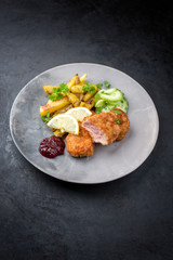 Traditionelles frittiertes Kalbssteak mit Bratkartoffel und Gurkensalat angeboten als closeup auf einem Modern design Teller mit Textfreiraum