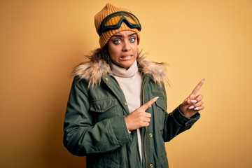 Young african american afro skier girl wearing snow sportswear and ski goggles Pointing aside worried and nervous with both hands, concerned and surprised expression