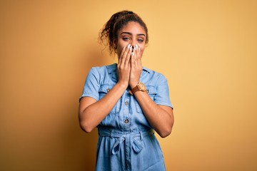 Young beautiful african american girl wearing denim dress standing over yellow background laughing...