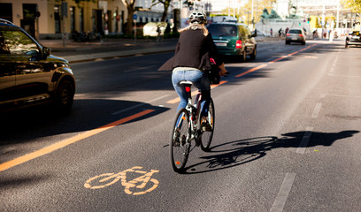 Cycle lane with orange painted bike on asphalt. Bicycle lane and car traffic. Ecological green urban transport. Fahrradspur und Autoverkehr. Fahrrad Zeichen auf Straße. Ökologischer urbaner Verkehr. - obrazy, fototapety, plakaty