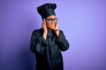 Young african american chef girl wearing cooker uniform and hat over purple background covering ears with fingers with annoyed expression for the noise of loud music. Deaf concept.