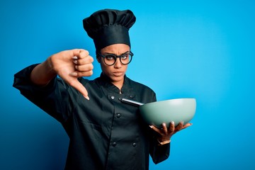 Young african american chef girl wearing cooker uniform and hat using whisk and bowl with angry...
