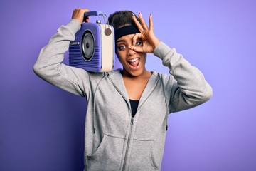 Young african american afro girl listening to music holding vintage radio over purple background with happy face smiling doing ok sign with hand on eye looking through fingers