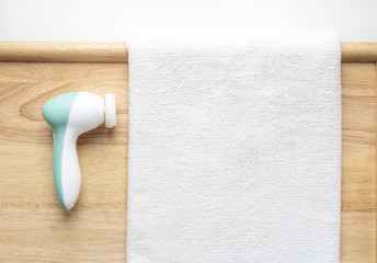 Massager brush for cleaning the skin of the face with a massage nozzle on a wooden background next to a white towel. Personal care at home.
