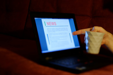 male hand with a mug with coffee and news on a laptop.