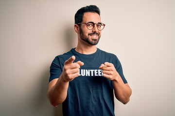 Handsome man with beard wearing t-shirt with volunteer message over white background pointing...