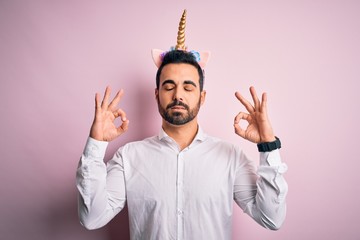 Young handsome man with beard wearing funny unicorn diadem over pink background relax and smiling with eyes closed doing meditation gesture with fingers. Yoga concept. © Krakenimages.com