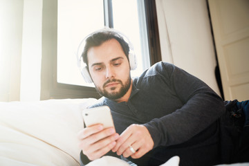 Attractive smart young man sitting on a sofa in the living room and using his smartphone. Relaxing time.