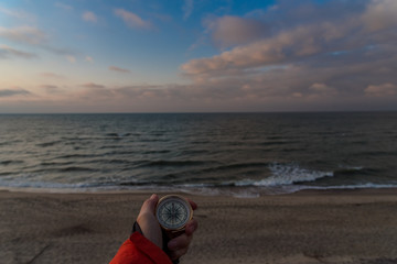 First-person view of a female hand with a compass on a background of a beautiful sea landscape. The concept of navigating the search for your own path and orientation to the cardinal points