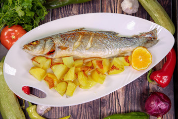 Tasty European bass with sauteed potatoes on a plate on a wooden table. Top view