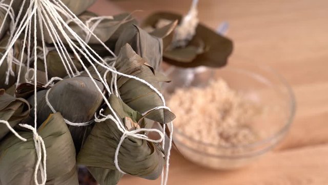 Making Zongzi - Family Preparing, Wrapping Bunch Of Chinese Rice Dumpling Zongzi Food Together On Wooden Table At Home For Dragon Boat Festival Celebration, Close Up, Lifestyle.