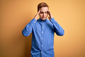 Young handsome redhead man wearing casual striped shirt over isolated yellow background with hand on head for pain in head because stress. Suffering migraine.