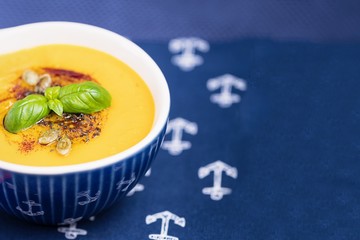 Homemade pumpkin cream soup with pumpkin seeds, pumpkin oil, basil leaf and turmeric on a blue background