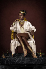 A gorgeous young female Egyptian Pharaoh wearing elegant clothing, a gold crown and jewelry is sitting on her golden throne.