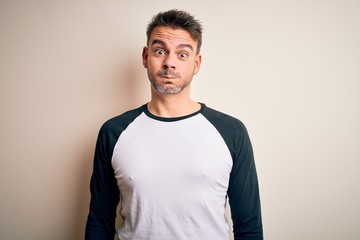 Young handsome man wearing casual t-shirt standing over isolated white background puffing cheeks with funny face. Mouth inflated with air, crazy expression.
