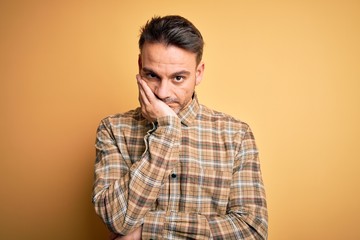 Obraz premium Young handsome man wearing casual shirt standing over isolated yellow background thinking looking tired and bored with depression problems with crossed arms.