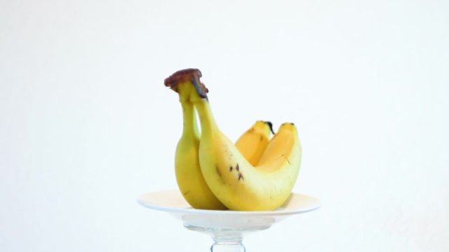 The yellow banana is spinning. Lies on a white saucer. White background. Ripe fruit. Vitamins close up