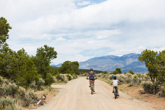 rear view of mother and young son on mountain bikes biking down dirt road