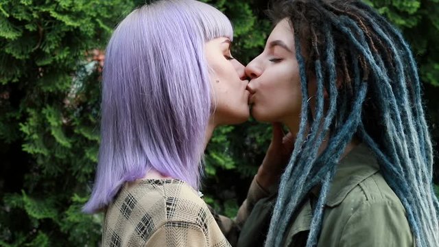 Lesbian LGBT female kiss outdoors in the sunlight. Beautiful pretty millennial girlfriends kissing each other in the sunlight outdoors. woman with dreadlocks.