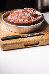 Homemade chocolate cake cooked on a domestic kitchen on a metal plate with a knife on a wood cutting board