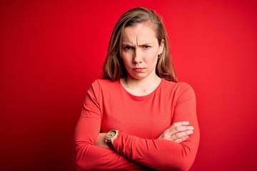 Young beautiful blonde woman wearing casual t-shirt standing over isolated red background skeptic and nervous, disapproving expression on face with crossed arms. Negative person.